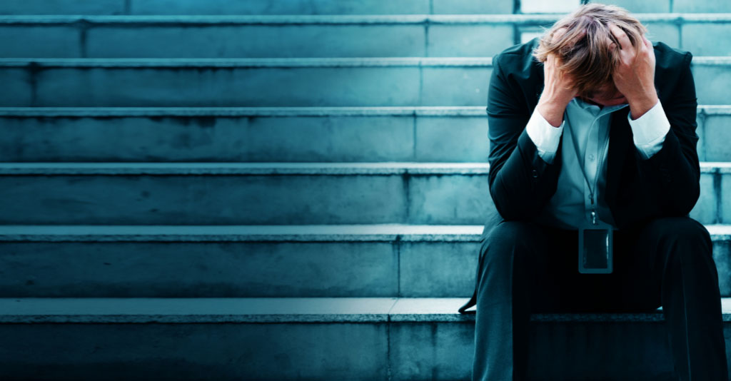 Image of a businessman in a suit, sitting on steps, with hands on his head in distress.
