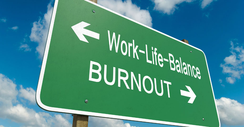 Green highway sign with sky background. The sign says "Work-Life-Balance" with an arrow to the left, and "Burnout" with an arrow to the right.