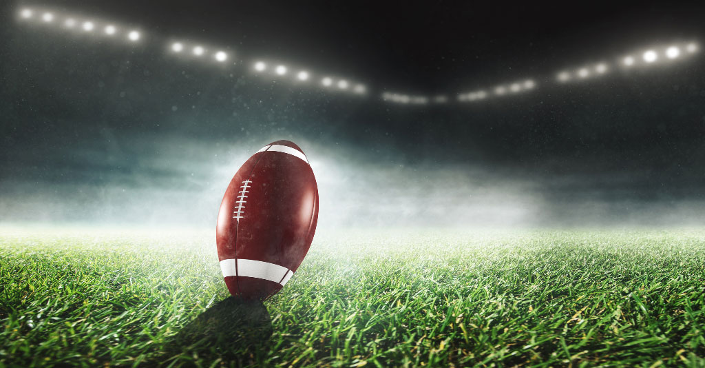 Image of a football on the field of a stadium at night with fog and lights.
